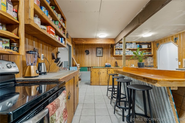 interior space featuring black electric range oven, light tile patterned flooring, and wooden walls