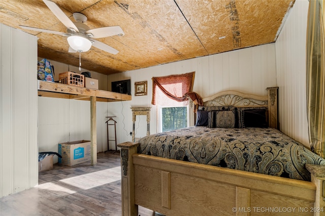 bedroom featuring wood walls, wood-type flooring, and ceiling fan