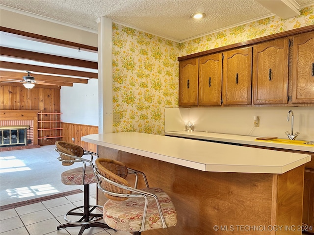 kitchen with sink, a textured ceiling, a brick fireplace, beamed ceiling, and light tile patterned floors