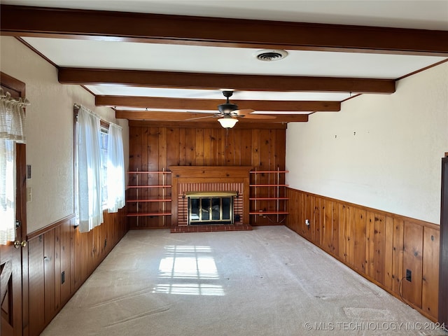 unfurnished living room with beam ceiling, wood walls, and a fireplace