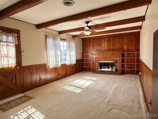 unfurnished living room with a brick fireplace, light carpet, ceiling fan, wooden walls, and beam ceiling