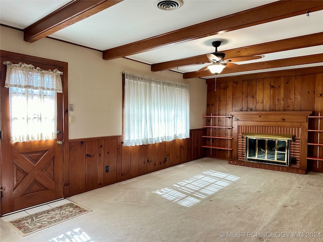 unfurnished living room with beam ceiling, wood walls, and carpet