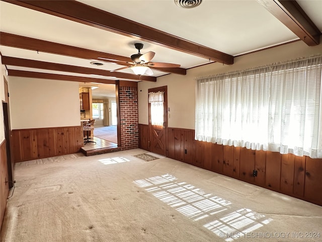 carpeted spare room with beam ceiling, wood walls, and ceiling fan