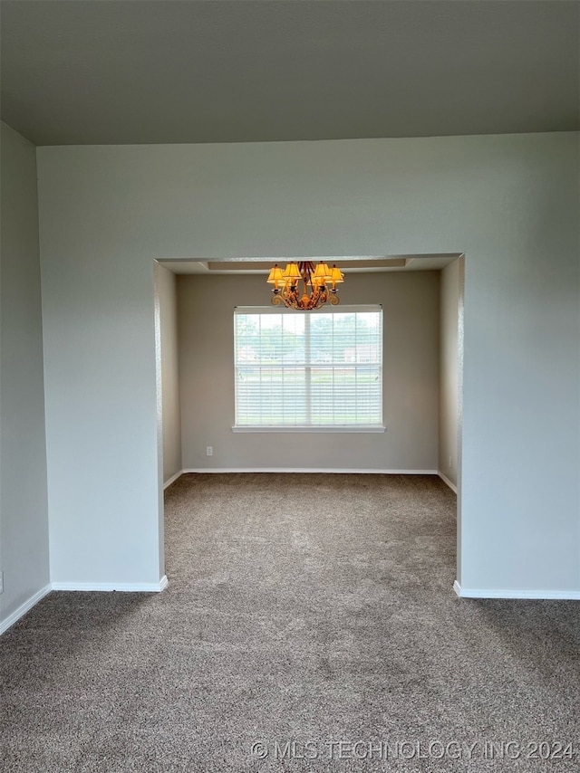 carpeted spare room with a notable chandelier