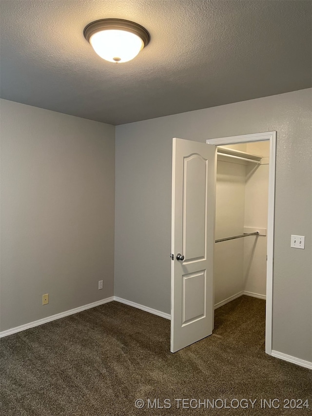 unfurnished bedroom with a closet, a textured ceiling, a spacious closet, and dark colored carpet