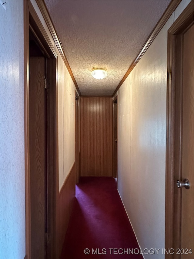 hallway featuring ornamental molding, dark colored carpet, a textured ceiling, and wood walls