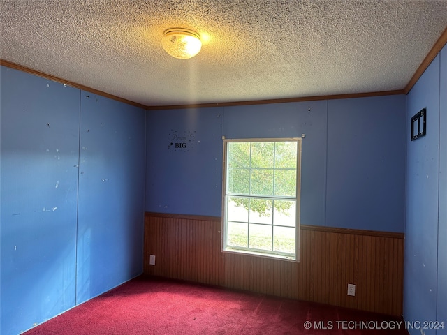 carpeted spare room featuring ornamental molding, a textured ceiling, and wooden walls