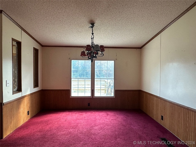 carpeted empty room with crown molding, a textured ceiling, wooden walls, and a notable chandelier