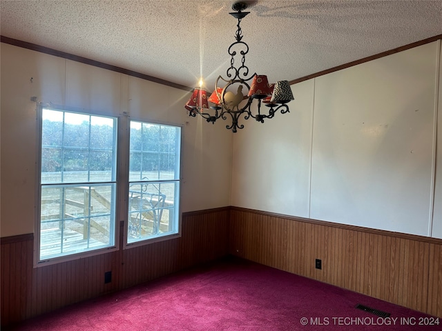 carpeted empty room featuring crown molding, wood walls, a textured ceiling, and a chandelier