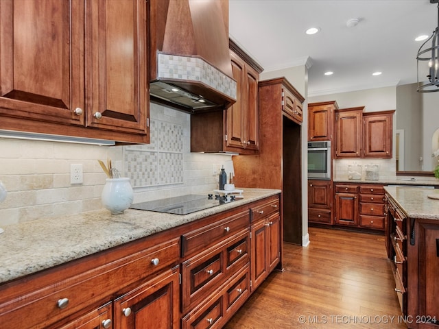 kitchen featuring black electric stovetop, stainless steel oven, pendant lighting, custom exhaust hood, and light hardwood / wood-style flooring