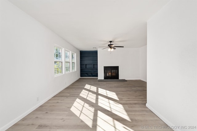 unfurnished living room with built in features, light wood-type flooring, and ceiling fan