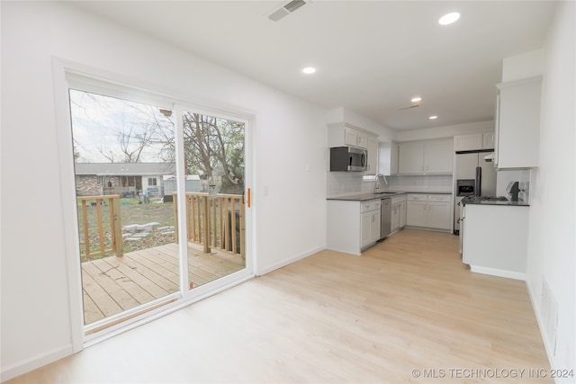 kitchen featuring appliances with stainless steel finishes, sink, white cabinets, decorative backsplash, and light hardwood / wood-style flooring