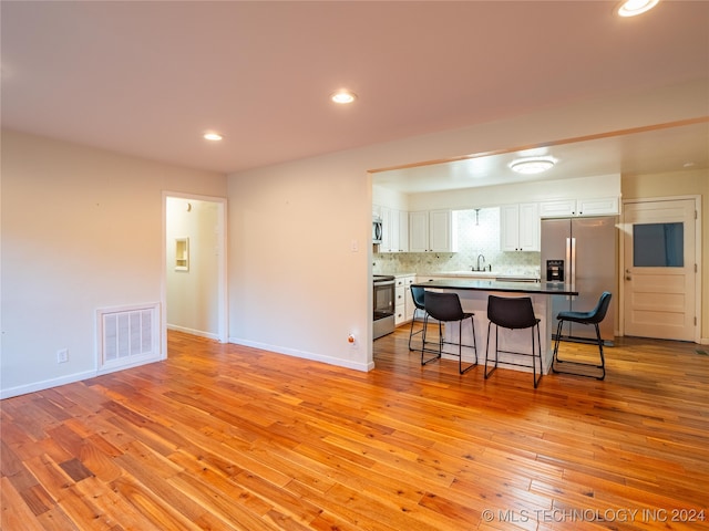 kitchen featuring appliances with stainless steel finishes, light hardwood / wood-style flooring, a breakfast bar area, and white cabinets