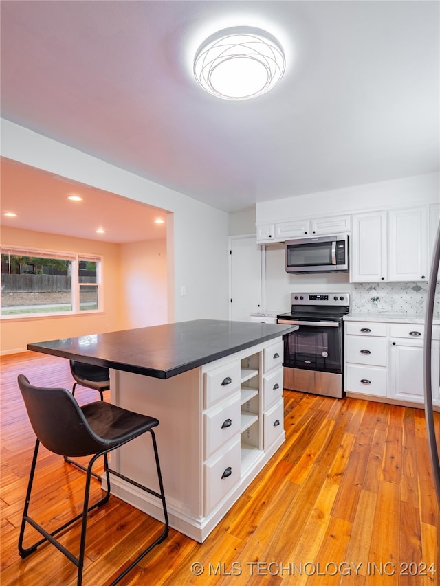 kitchen with a breakfast bar area, a center island, light wood-type flooring, white cabinetry, and appliances with stainless steel finishes