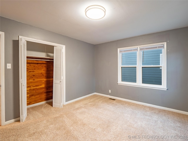 unfurnished bedroom featuring light colored carpet, a closet, and wood walls