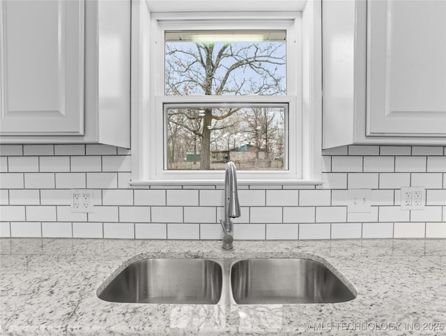 interior details featuring tasteful backsplash, light stone countertops, sink, and white cabinetry