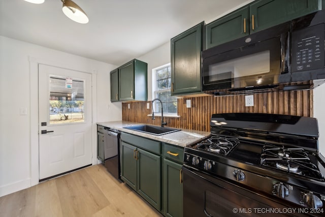 kitchen with light stone countertops, black appliances, light hardwood / wood-style floors, sink, and green cabinetry