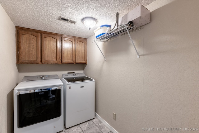 laundry room featuring cabinets, a textured ceiling, washer and clothes dryer, and light tile patterned floors