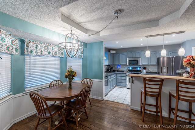 dining room with an inviting chandelier, a tray ceiling, a textured ceiling, and light hardwood / wood-style floors