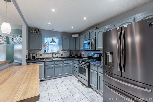 kitchen with stainless steel appliances, sink, light tile patterned floors, pendant lighting, and decorative backsplash