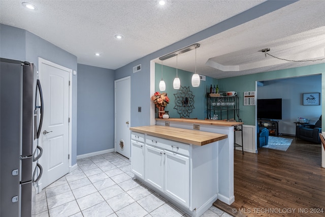 kitchen featuring wooden counters, white cabinetry, stainless steel refrigerator, hanging light fixtures, and light hardwood / wood-style floors