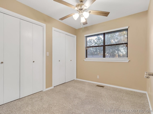 unfurnished bedroom with ceiling fan, two closets, and light colored carpet