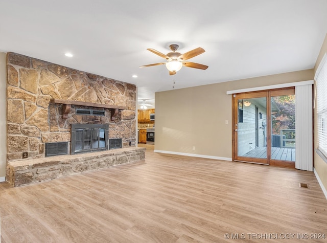 unfurnished living room with ceiling fan, a stone fireplace, and light wood-type flooring