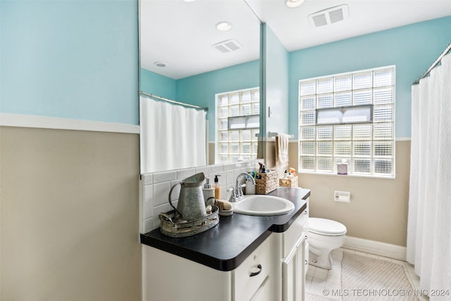 bathroom with a healthy amount of sunlight, vanity, backsplash, and toilet