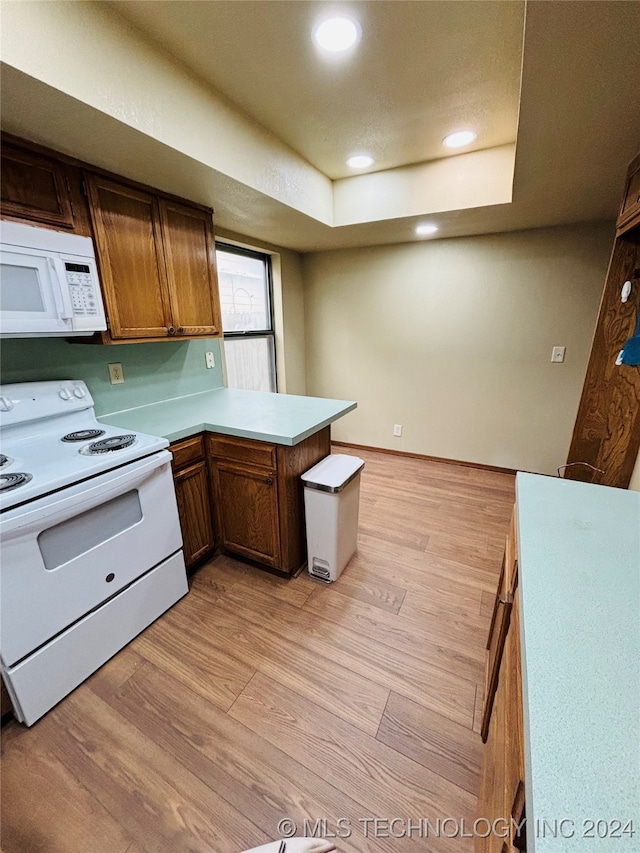 kitchen featuring kitchen peninsula, light wood-type flooring, white appliances, and a raised ceiling