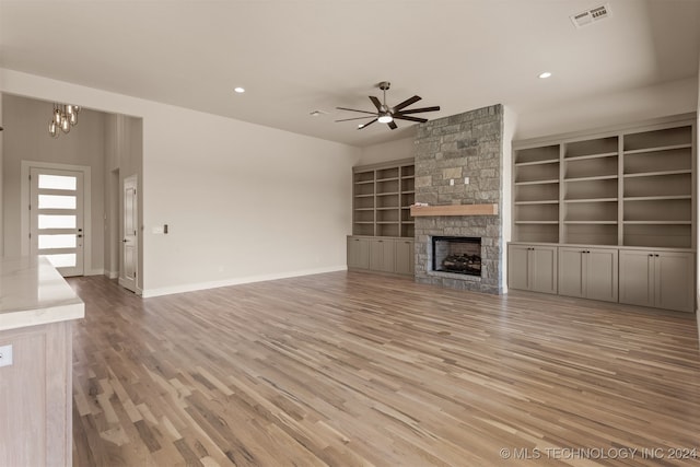 unfurnished living room featuring ceiling fan with notable chandelier, light wood-type flooring, and a fireplace