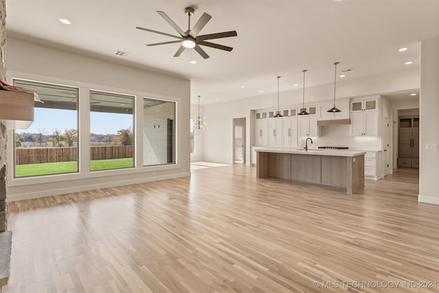 unfurnished living room with sink, ceiling fan with notable chandelier, and light wood-type flooring