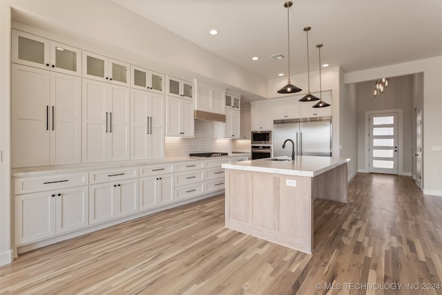 kitchen with white cabinetry, a kitchen island with sink, sink, built in appliances, and decorative light fixtures