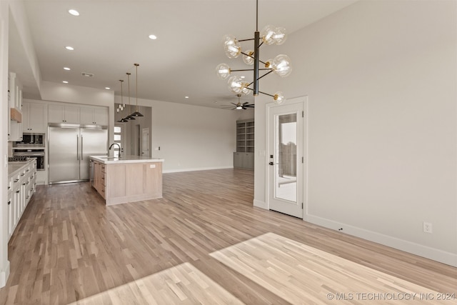 kitchen featuring an island with sink, appliances with stainless steel finishes, white cabinetry, light hardwood / wood-style flooring, and pendant lighting