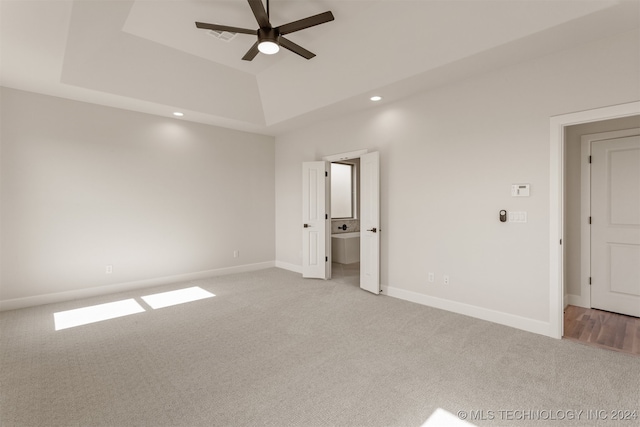 unfurnished bedroom featuring ceiling fan, light carpet, and a tray ceiling