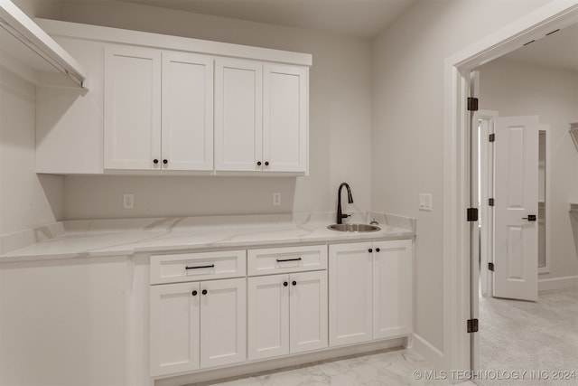 bar with sink, white cabinets, light stone counters, and light carpet