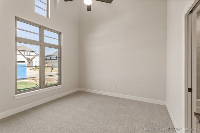 empty room with a wealth of natural light, carpet floors, a towering ceiling, and ceiling fan