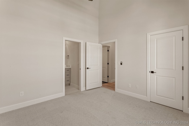 unfurnished bedroom with ensuite bathroom, light colored carpet, and a high ceiling