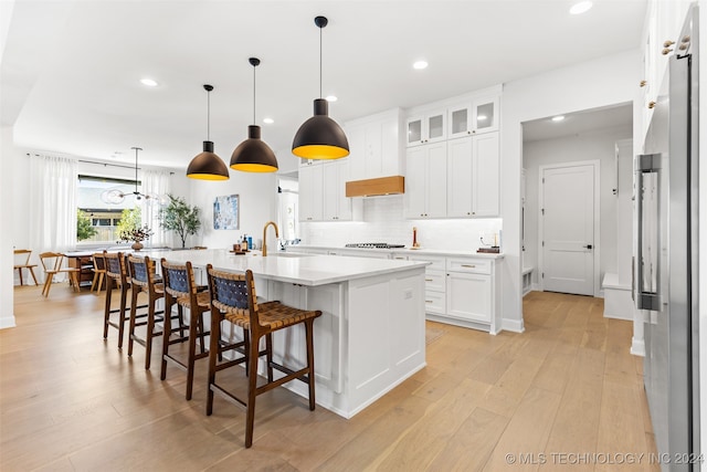 kitchen with white cabinets, an island with sink, light wood-type flooring, pendant lighting, and sink