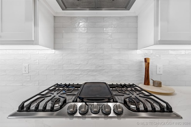 room details featuring decorative backsplash, white cabinets, light stone counters, and stainless steel gas cooktop