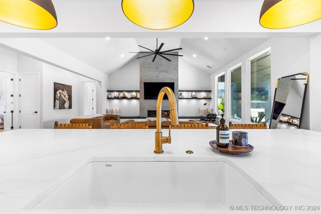 kitchen featuring light stone countertops, sink, vaulted ceiling, and a tile fireplace