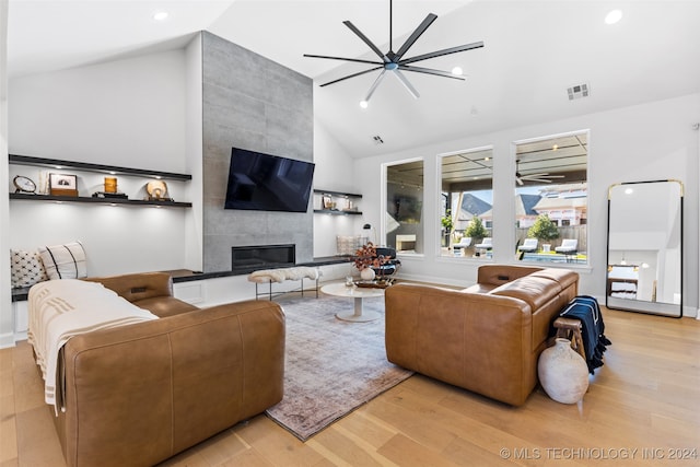 living room featuring ceiling fan, a tile fireplace, light wood-type flooring, and vaulted ceiling