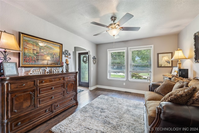 living room featuring dark wood-type flooring, a textured ceiling, and ceiling fan