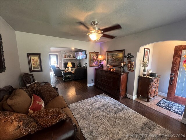 living room with ceiling fan, a textured ceiling, and dark hardwood / wood-style floors