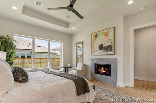 bedroom with a raised ceiling, a fireplace, light wood-type flooring, and ceiling fan