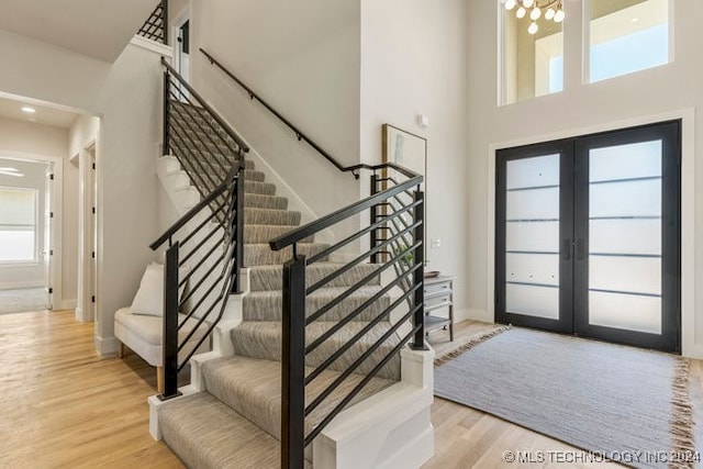 entryway featuring french doors, light hardwood / wood-style flooring, a high ceiling, and a chandelier