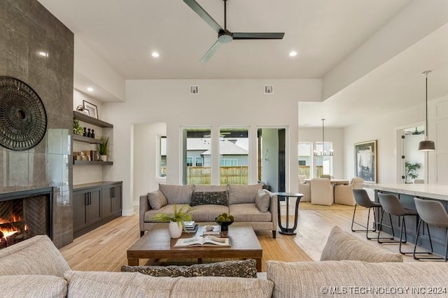 living room with light hardwood / wood-style floors, ceiling fan with notable chandelier, and a fireplace