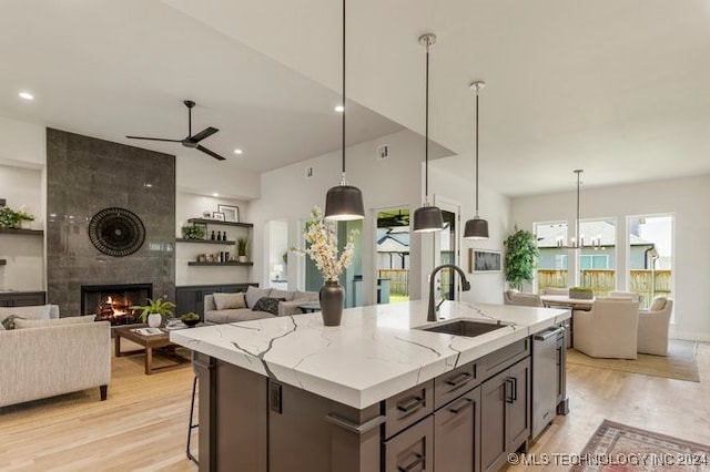 kitchen with a center island with sink, sink, light wood-type flooring, light stone counters, and a fireplace