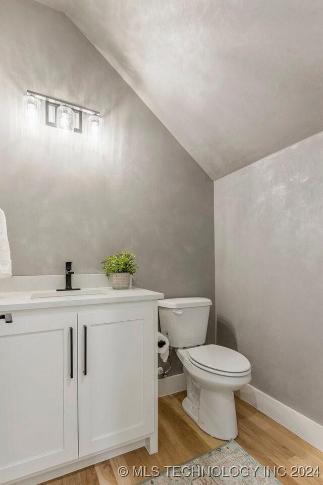 bathroom with vanity, hardwood / wood-style flooring, toilet, and vaulted ceiling