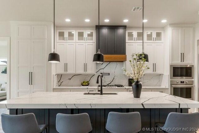 kitchen featuring appliances with stainless steel finishes, backsplash, a large island, pendant lighting, and light stone counters