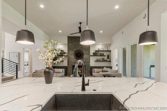 kitchen featuring sink, decorative light fixtures, light stone counters, and a tiled fireplace